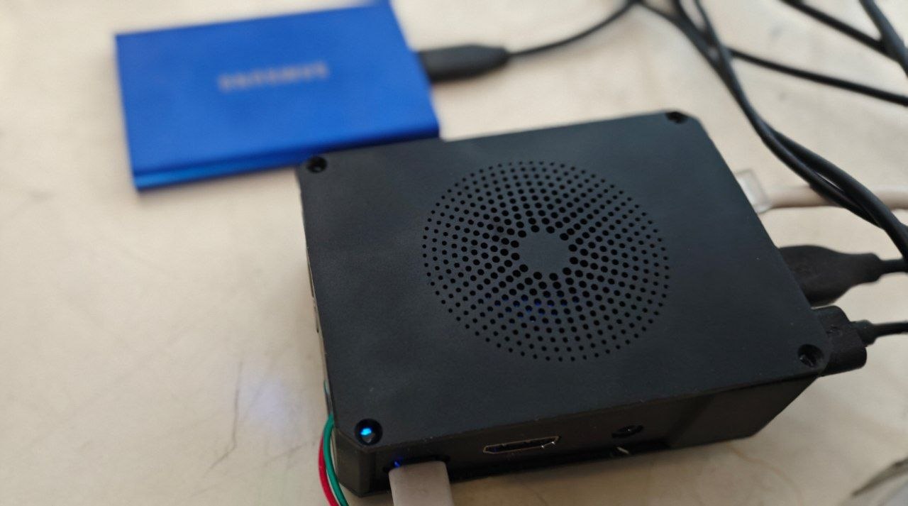 A Radxa ROCK 5C single-board computer in a black case, connected by USB to a blue Samsung T7 portable SSD.
